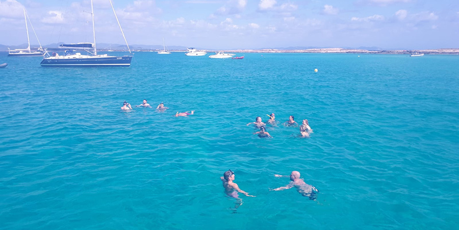 A group of people enjoy a swim in the ocean. There're boats in the distance.