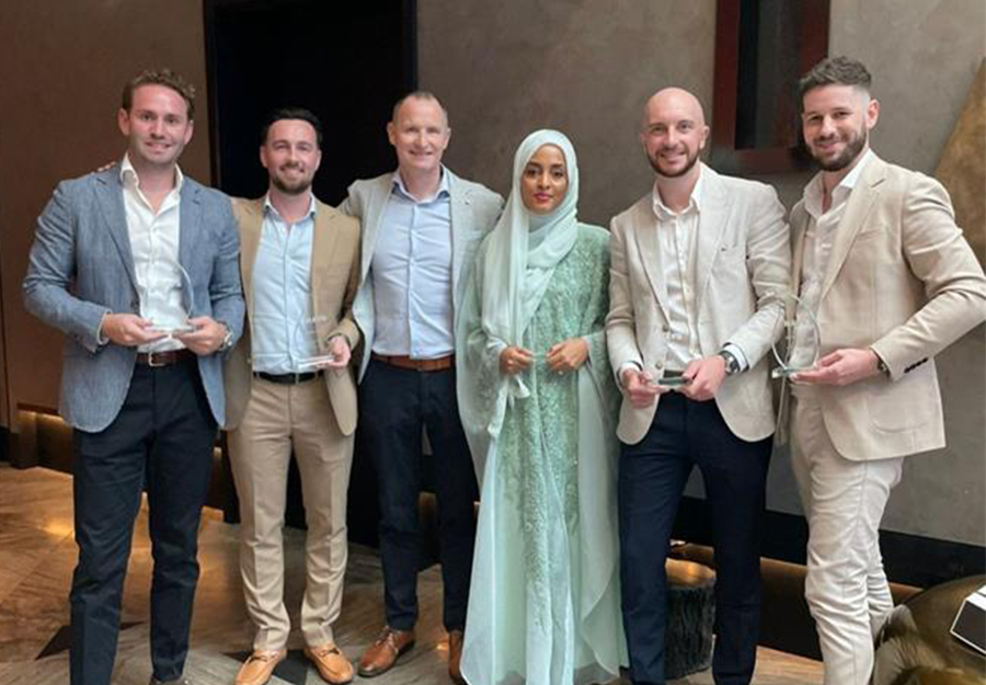 Three formally dressed gentlemen proudly display an award, smiling broadly for a group photo.