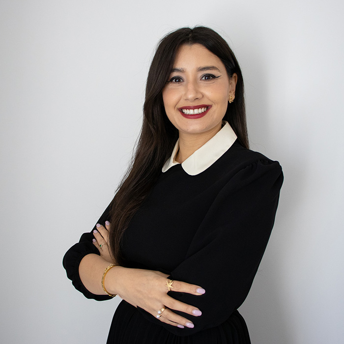 A woman in a black dress and white shirt standing confidently and smiling. 